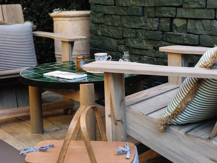 An outdoor seating area with a stone wall, a round table, and a cushioned bench.