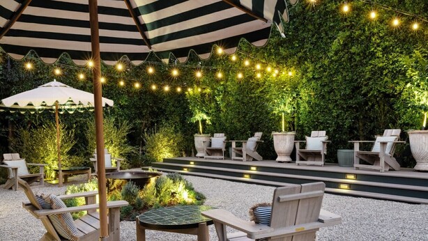 An outdoor patio with wooden furniture, a striped umbrella, and string lights. - Le Petit Pali Brentwood West Los Angeles (Los Angeles)