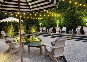 Un patio al aire libre con mobiliario de madera, un paraguas a rayas y luces colgantes.