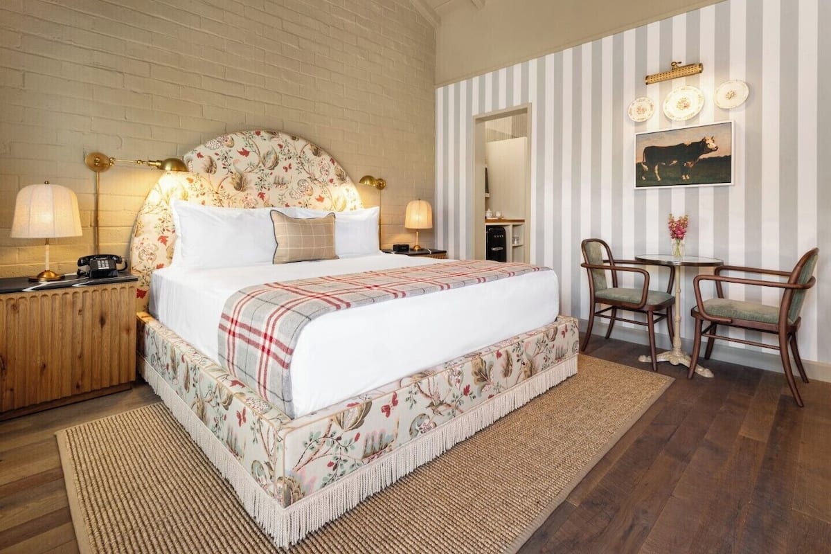 A bedroom with a large bed, a wooden nightstand, a desk with two chairs, and a striped wall.