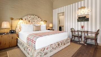 A bedroom with a large bed, a wooden nightstand, a desk with two chairs, and a striped wall.