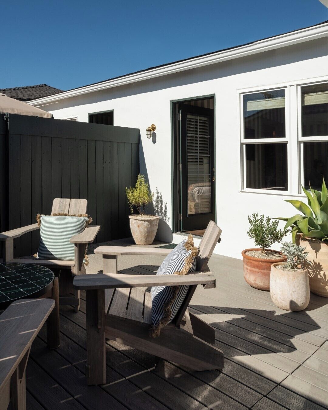 A patio with wooden furniture, including two chairs and a table, and several potted plants.