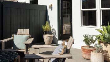 A patio with wooden furniture, including two chairs and a table, and several potted plants.