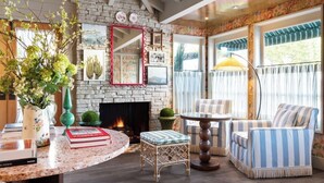 A cozy living room with a stone fireplace, a round coffee table, striped armchairs, and a bookshelf with books. - Le Petit Pali Brentwood West Los Angeles (Los Angeles)