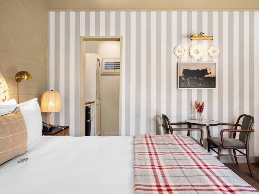 A hotel room with a bed, bedside table with lamp, a dining area with chairs, a table, and a wall-mounted plate rack.
