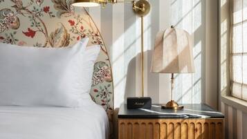 Un dormitorio con cama, mesita de noche, lámpara y ventana con persianas verticales.