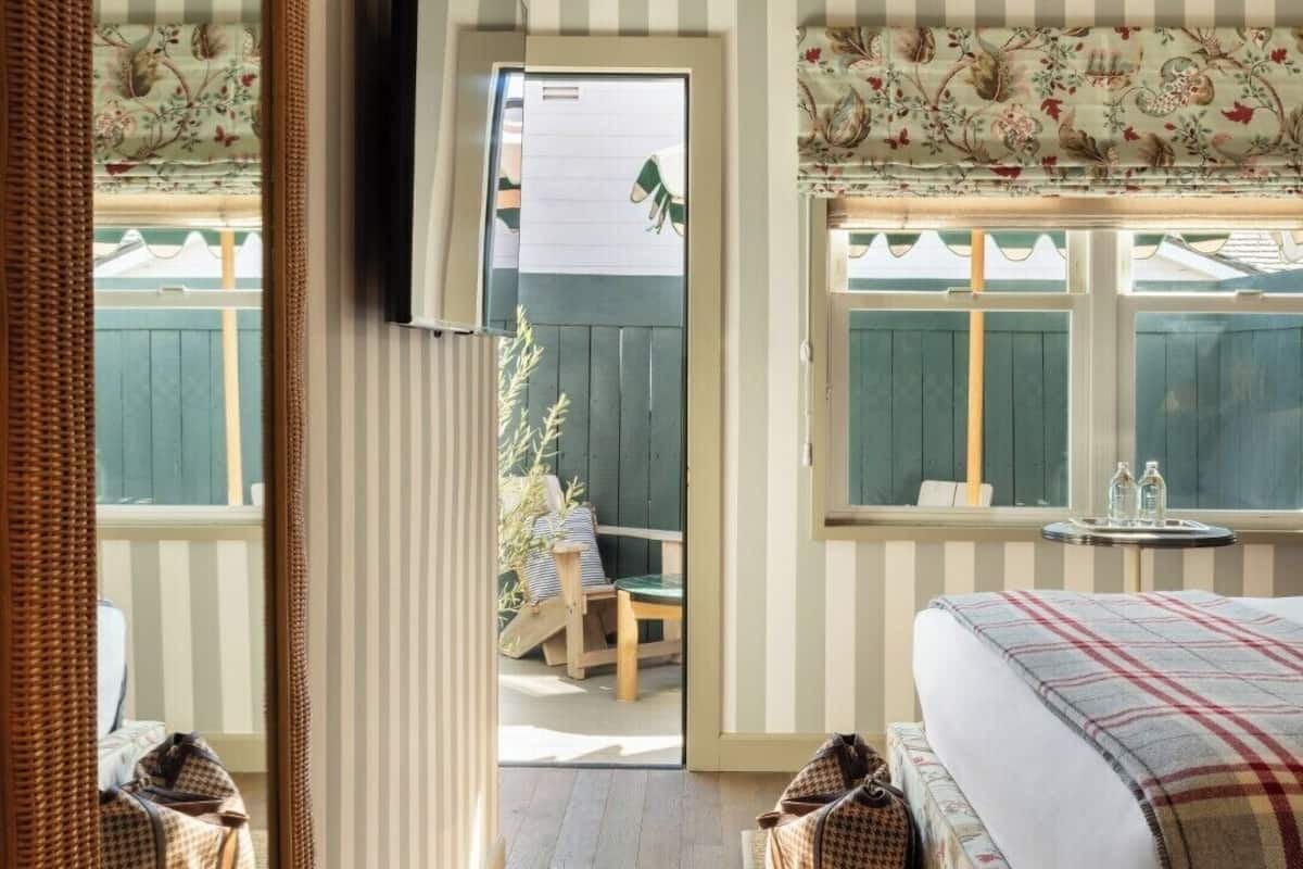 A bedroom with a bed, a mirror, a window, and a view of the outside.
