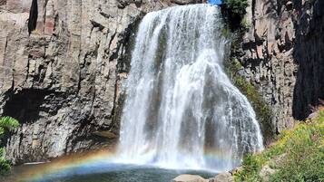 A waterfall cascading down a rocky cliff into a clear pool, surrounded by greenery and trees.