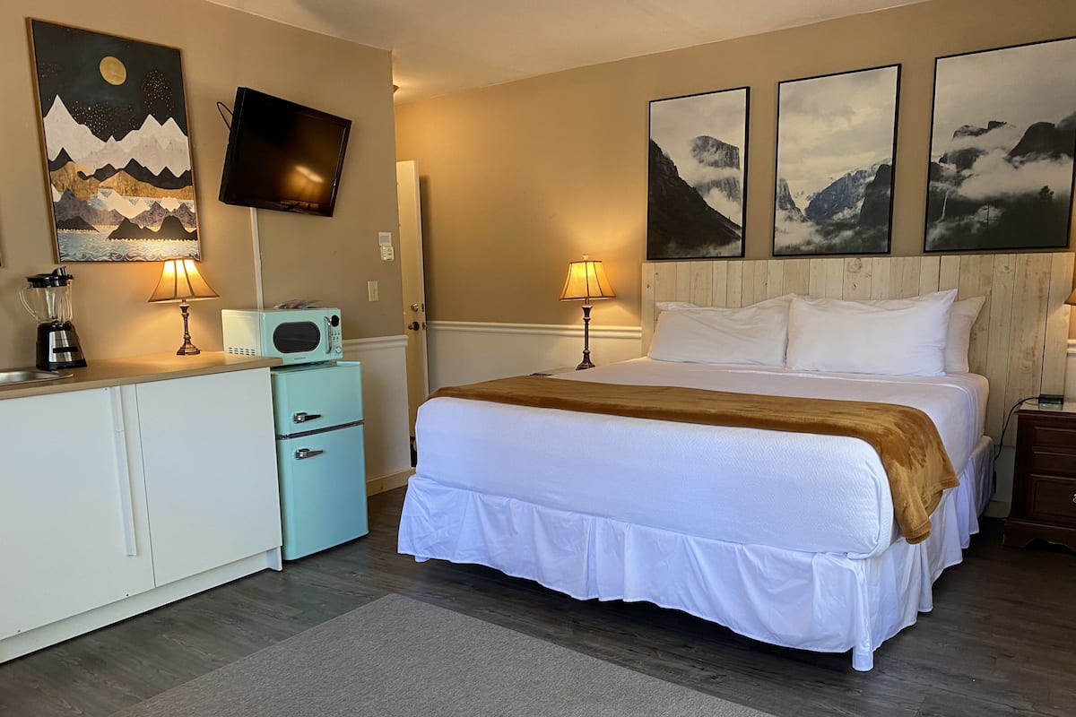 A hotel room with a bed, a desk, a microwave, a TV, and artwork on the walls.