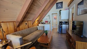 A cozy loft-style living space with a wooden ceiling, a sofa, a dining table, a kitchen area, and a TV. - Cinnamon Bear Inn (Mammoth Lakes)