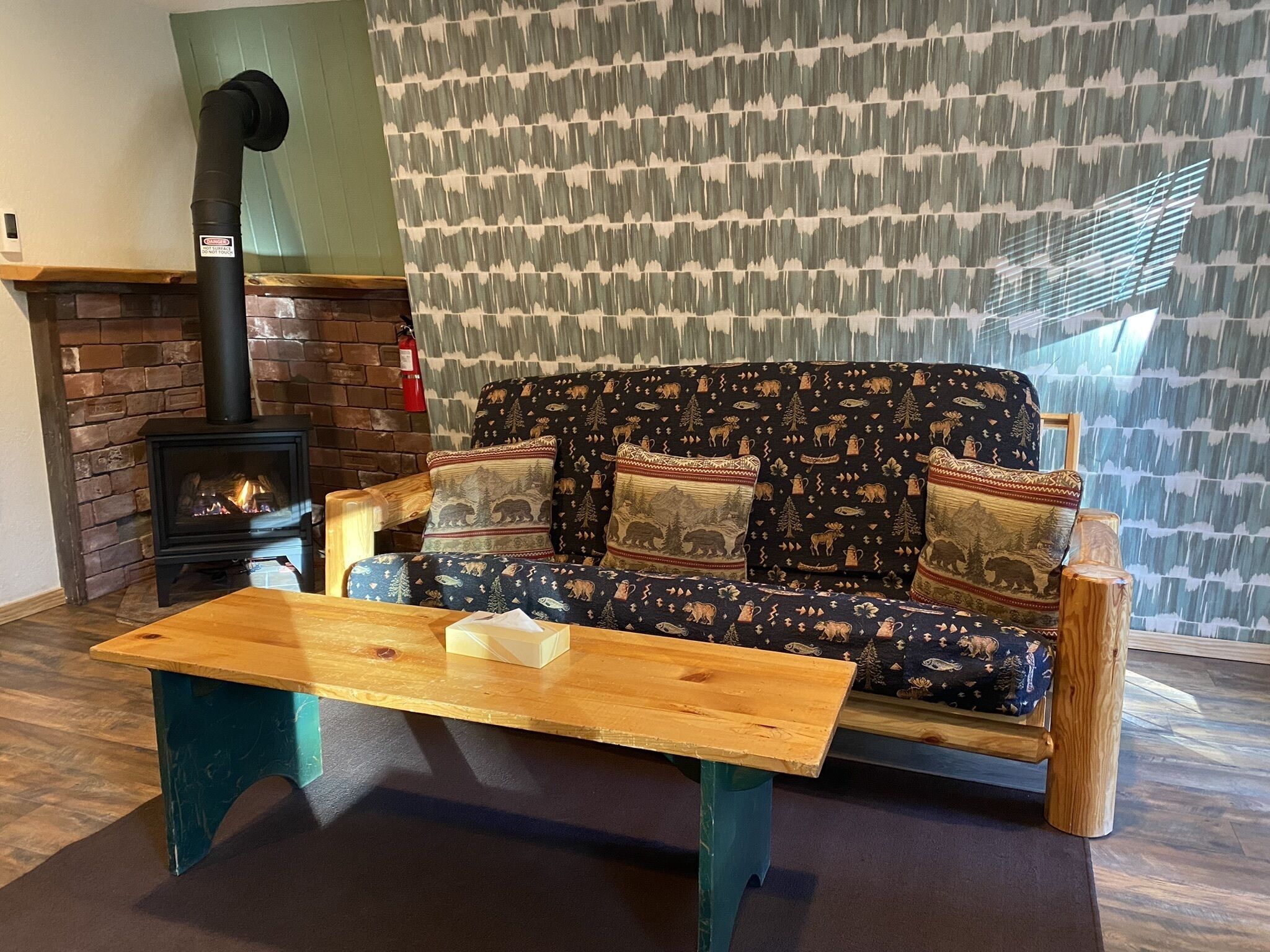 A cozy living room with a sofa, a wooden coffee table, a fireplace, and a patterned wall.