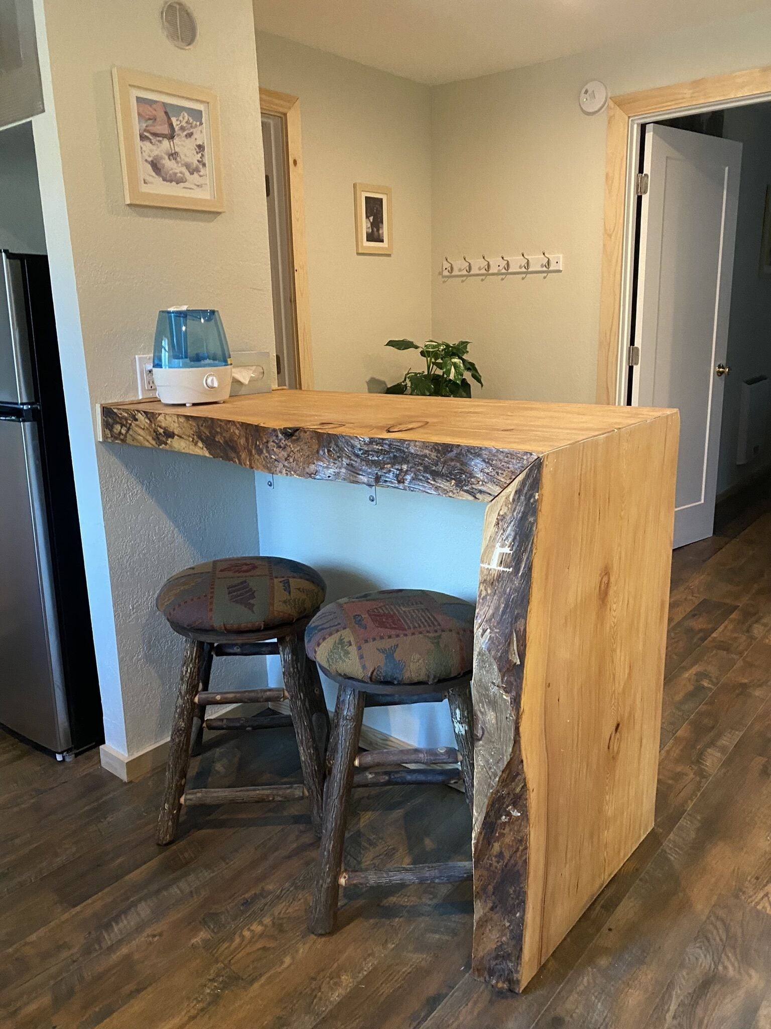 Una cocina con una isla de madera, dos taburetes, un refrigerador y una planta.
