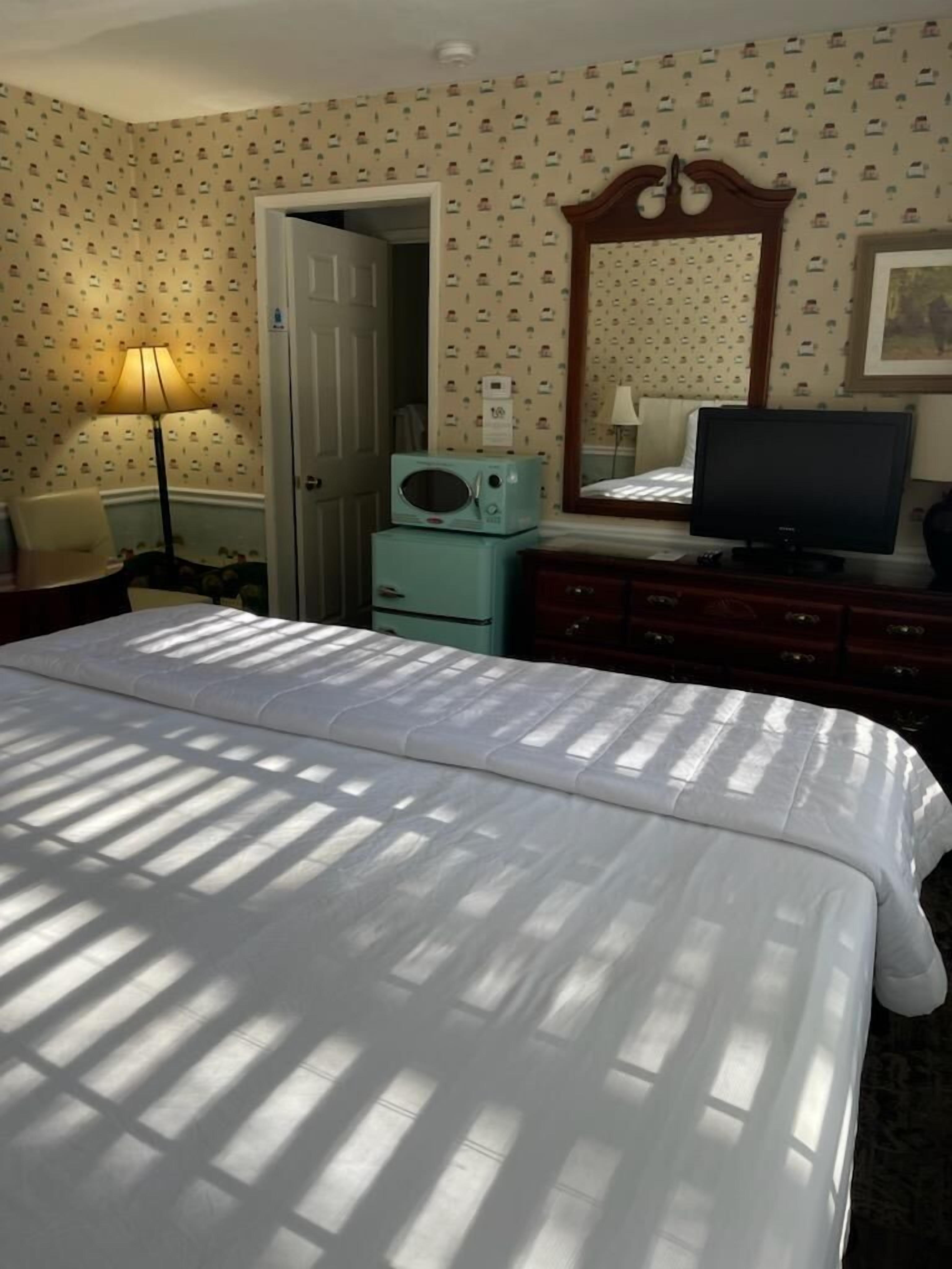 Ein Hotelzimmer mit einem großen Bett, einem Fernseher, einem Schminktisch, einer Mikrowelle und einer Tür zu einem weiteren Raum.