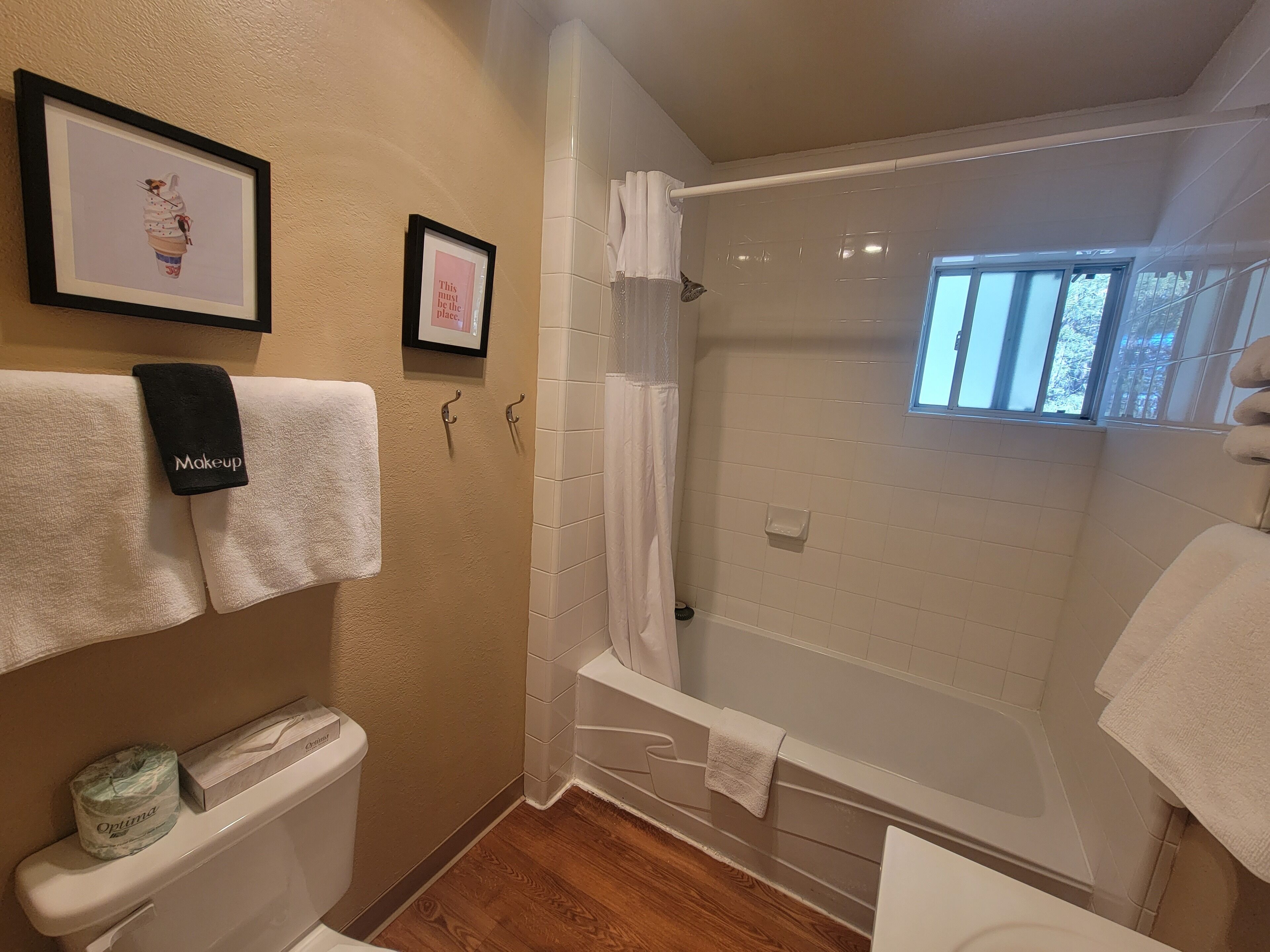 A bathroom with a bathtub, a toilet, and a shower. There are towels hanging on hooks and a framed picture on the wall.