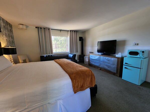 A hotel room with a large bed, a television, a small kitchenette, and a window with curtains.