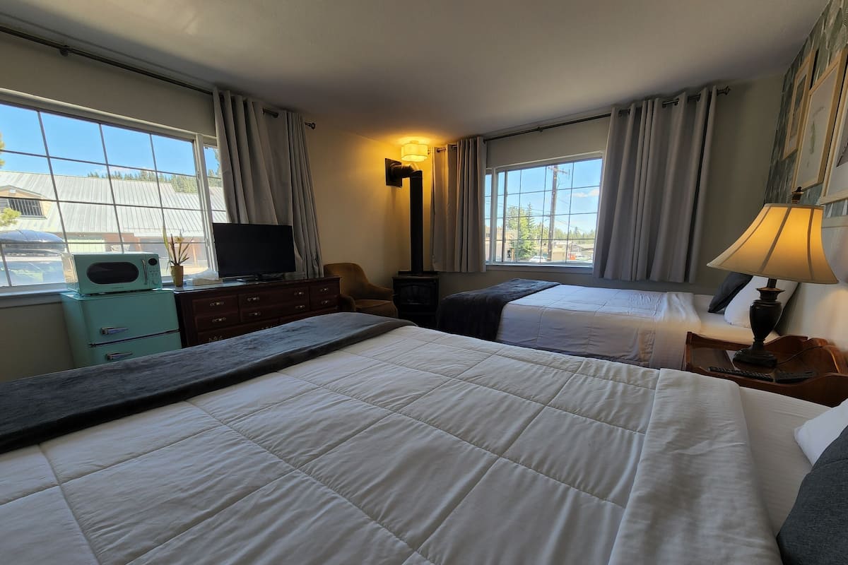 A hotel room with two beds, a television, a dresser, and a lamp.