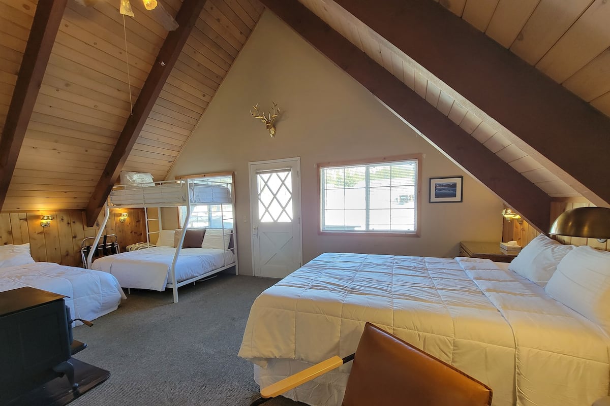 A cozy attic bedroom with bunk beds, a large bed, and a desk.
