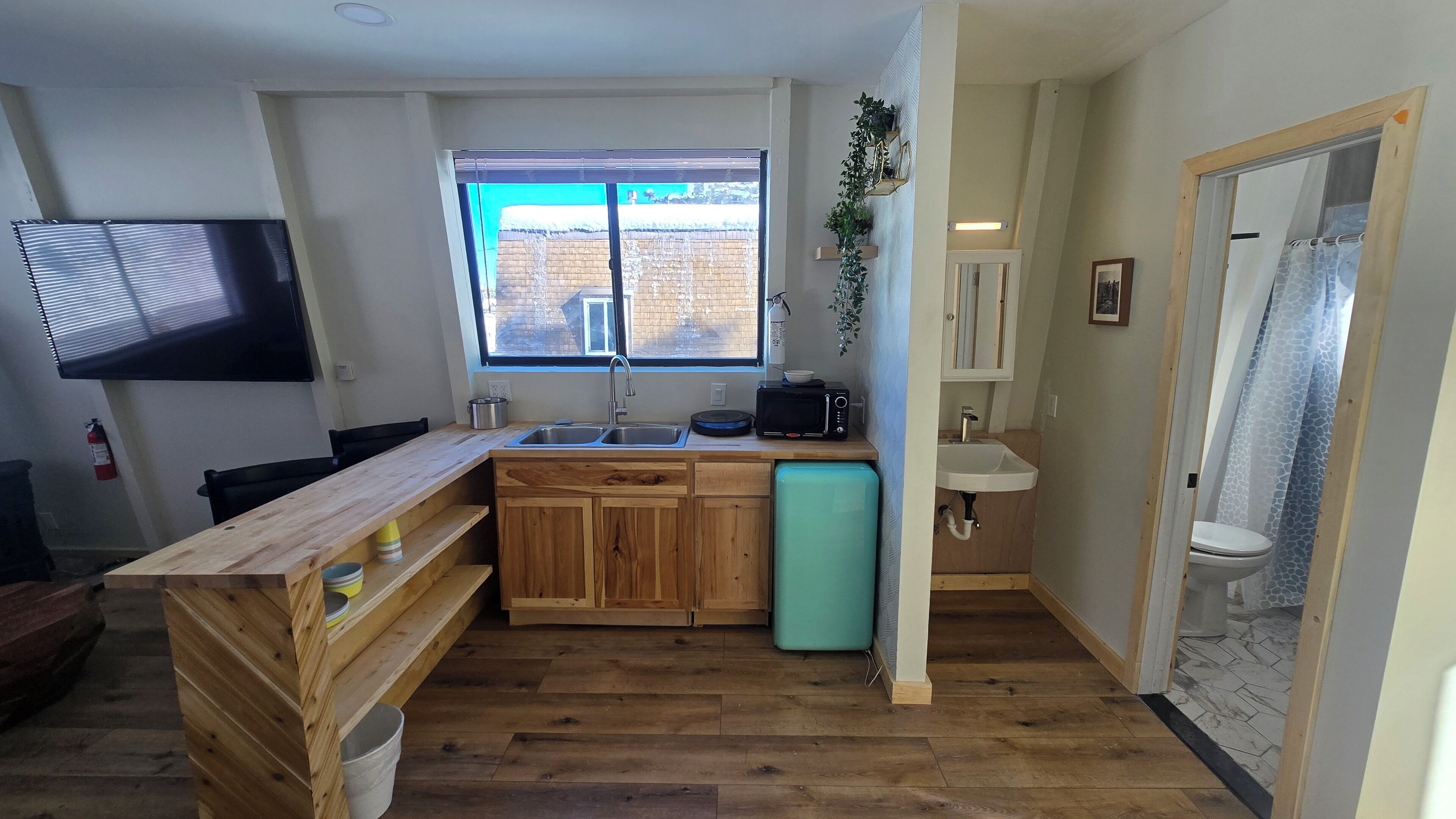 A compact kitchen with wooden cabinets, a sink, a microwave, and a window with a view of the outside.