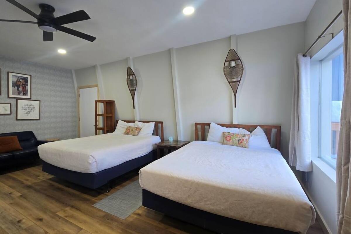 A hotel room with two single beds, a sofa, a ceiling fan, and framed pictures on the wall.