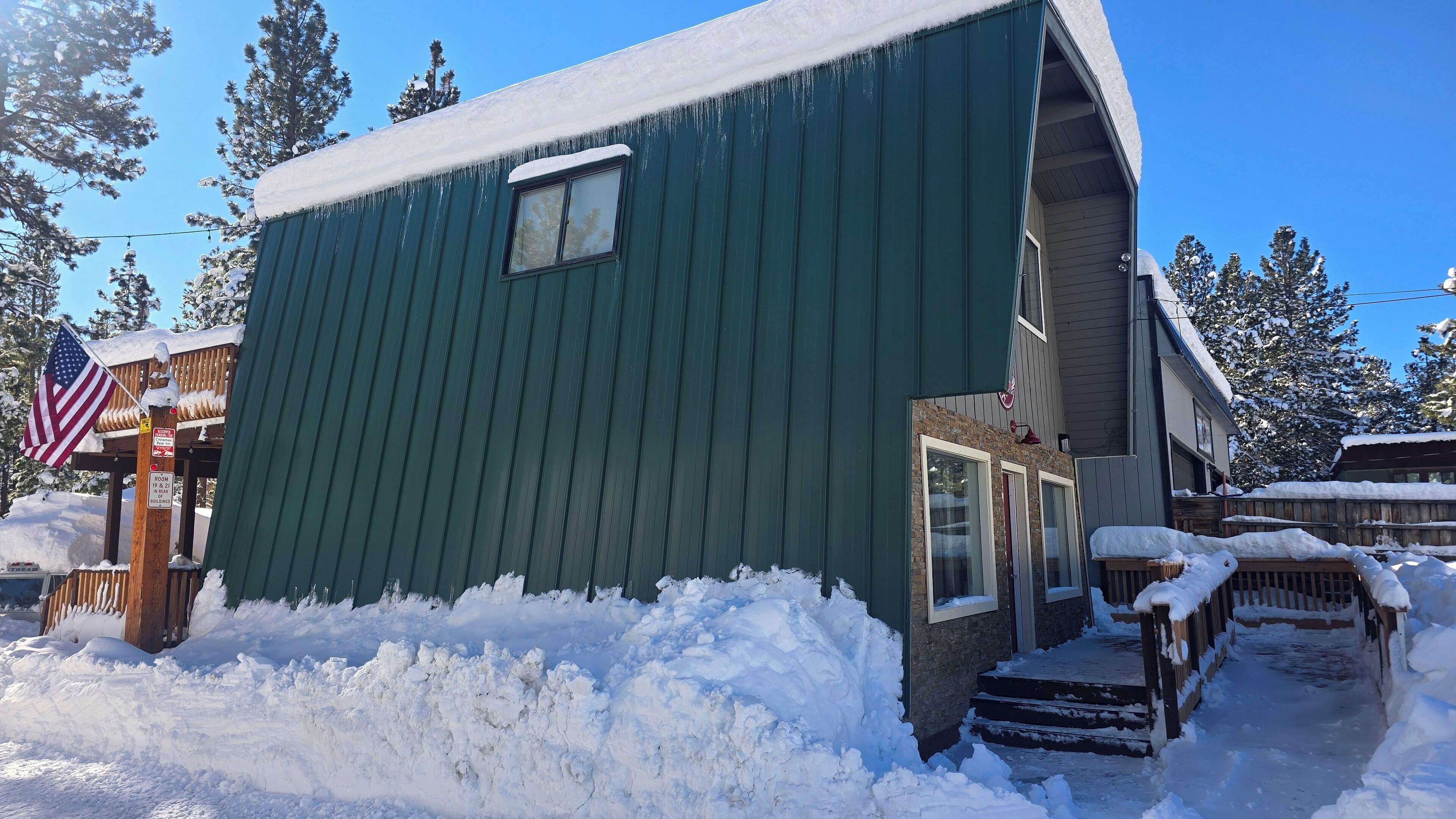 A green building with a small window and a door, surrounded by snow and trees.