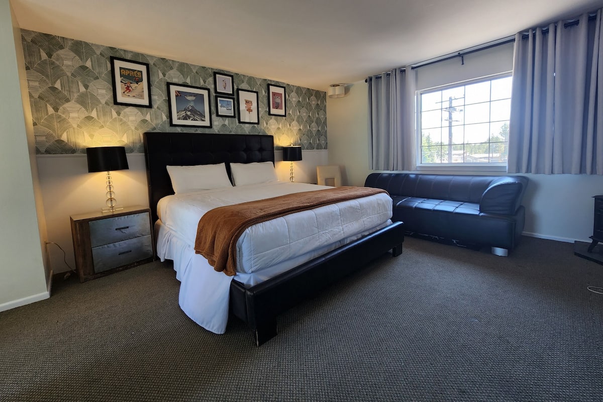 A hotel room with a large bed, a sofa, a window with curtains, and framed pictures on the wall.