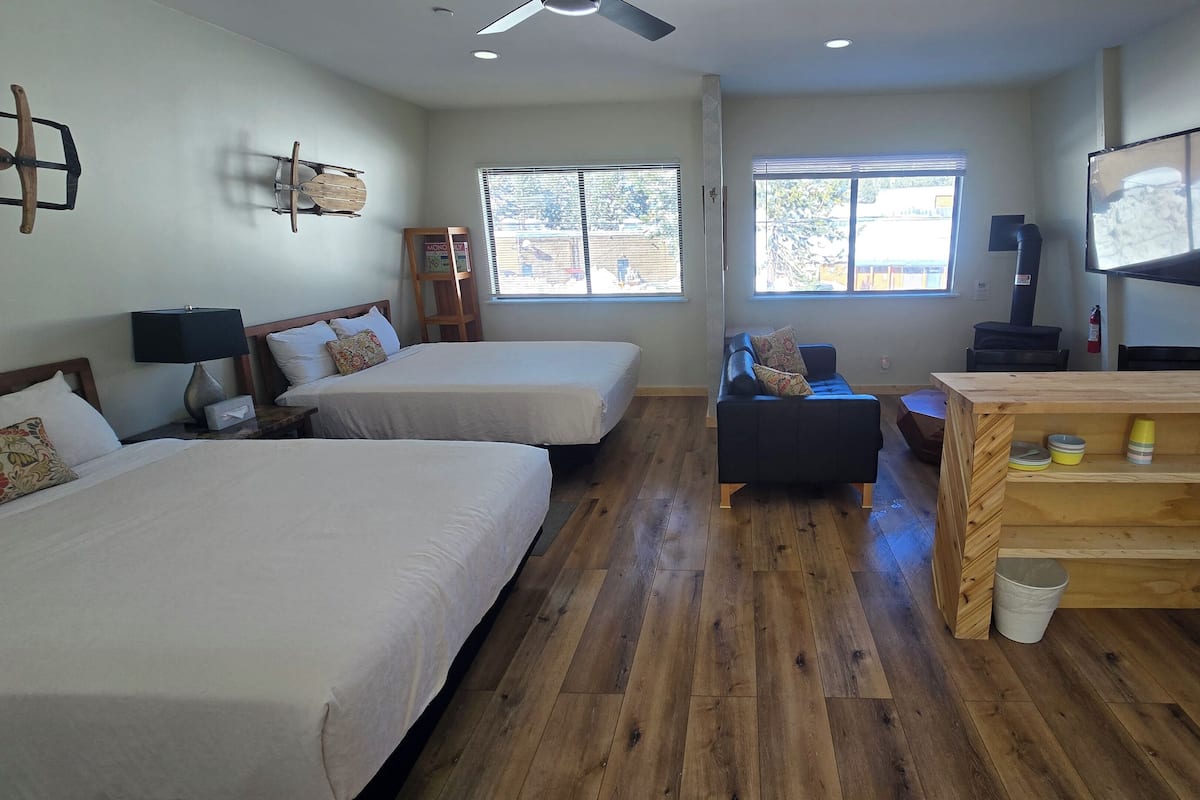 A hotel room with two beds, a wooden desk, a TV, and a window with a view of the outside.
