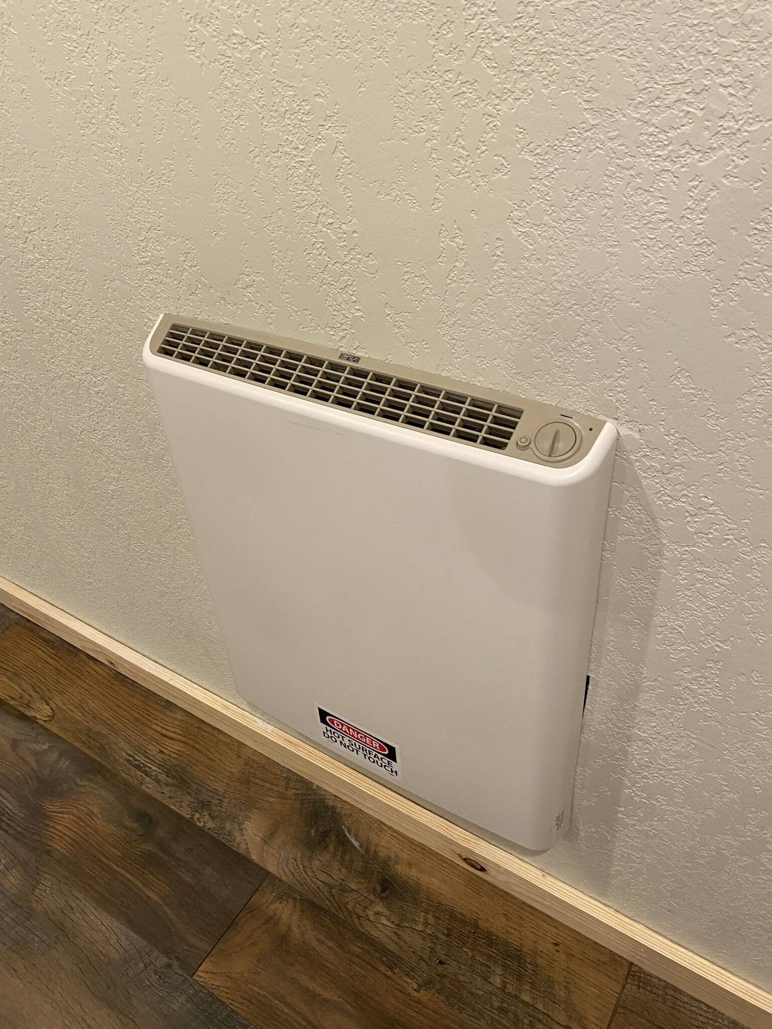 A white wall-mounted heater with a warning sign indicating it is hot to the touch.