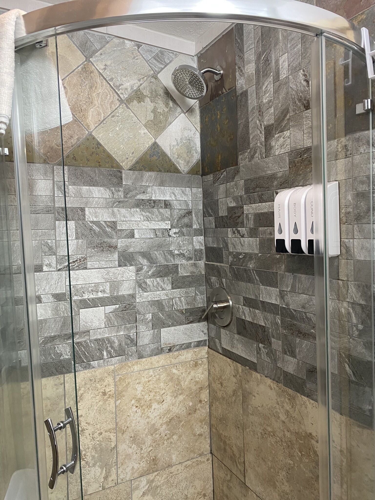 Eine Dusche mit Glastür, Wänden aus Steinplatten und einem Handtrockner.