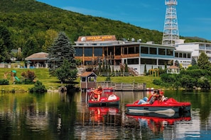 A lakeside view of a hotel with a dock, boats, and a mountain backdrop.