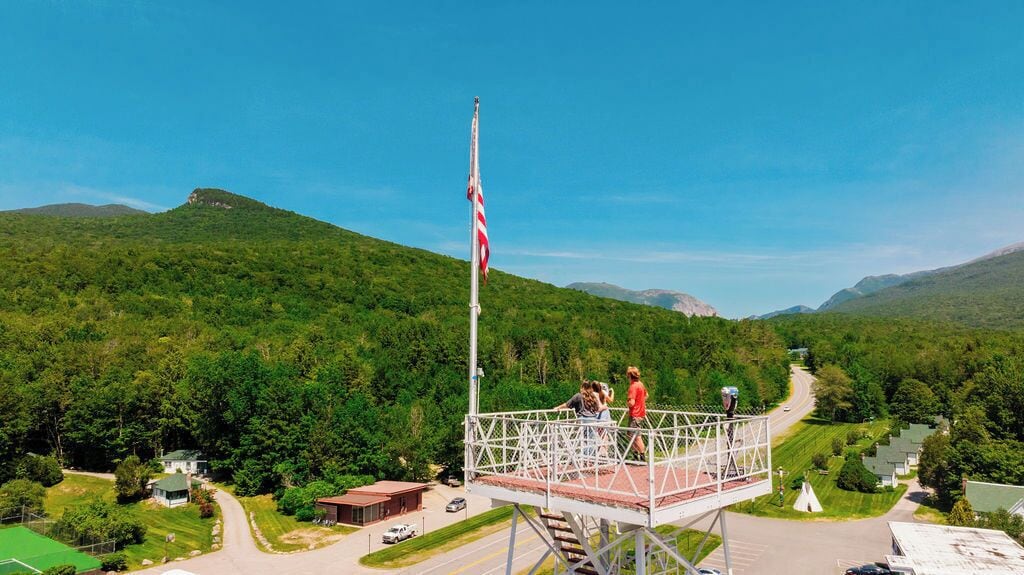 A scenic overlook with a flagpole, a metal walkway, and a road leading through a green landscape.