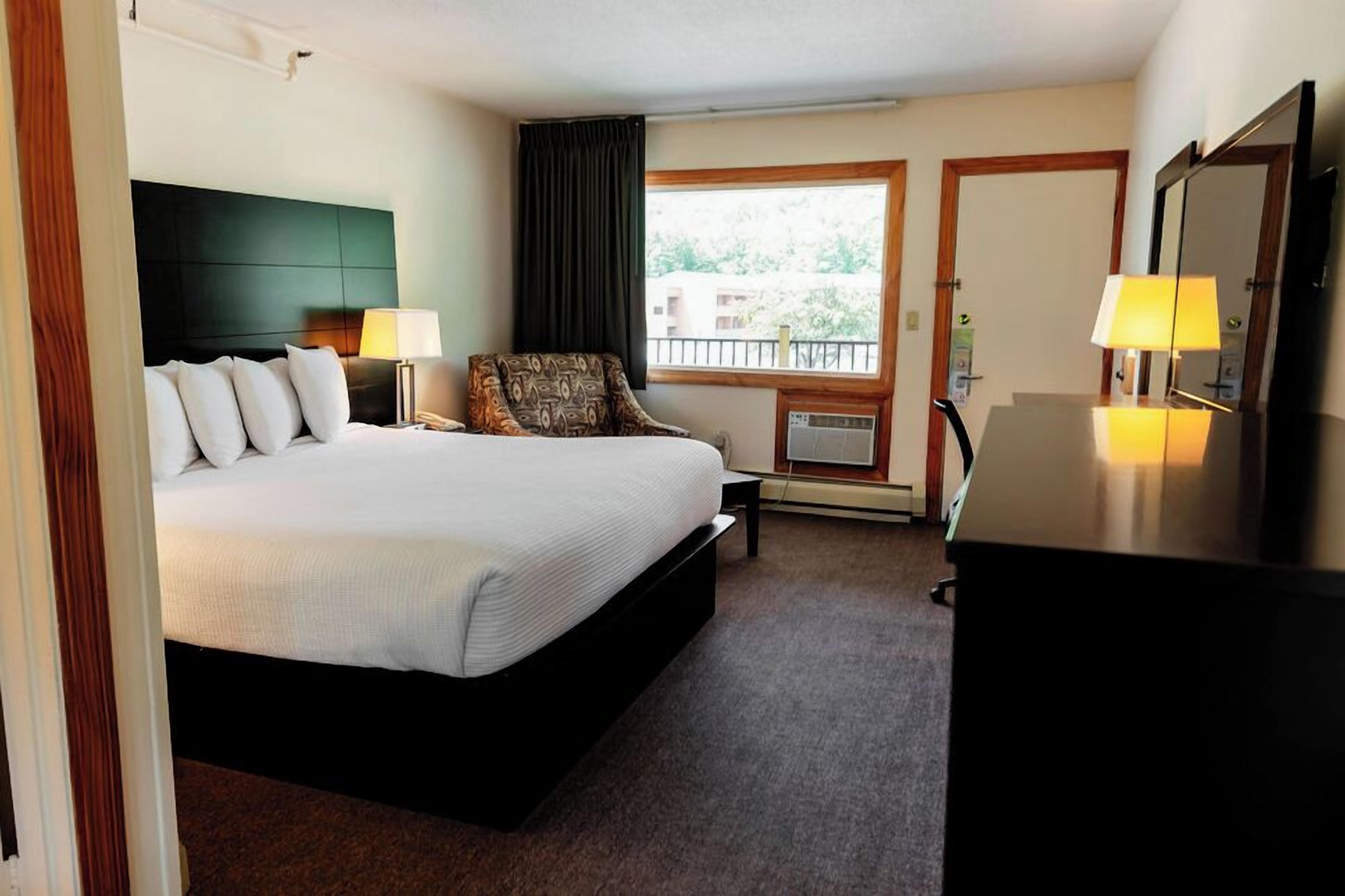 Une chambre d’hôtel comprenant un lit, des lampes de chevet, une chaise, un bureau et un téléviseur.
