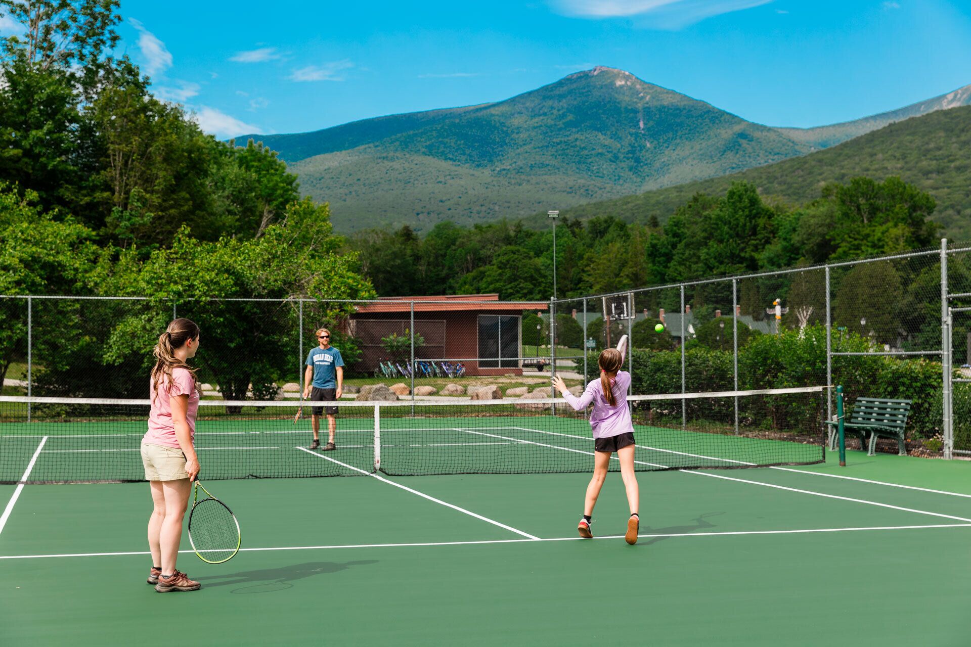 Una cancha de tenis con red, rodeada de árboles y montañas.
