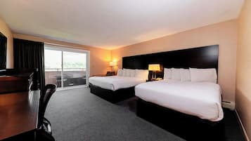 A hotel room with two beds, a desk, a chair, a lamp, and a view through a glass door.