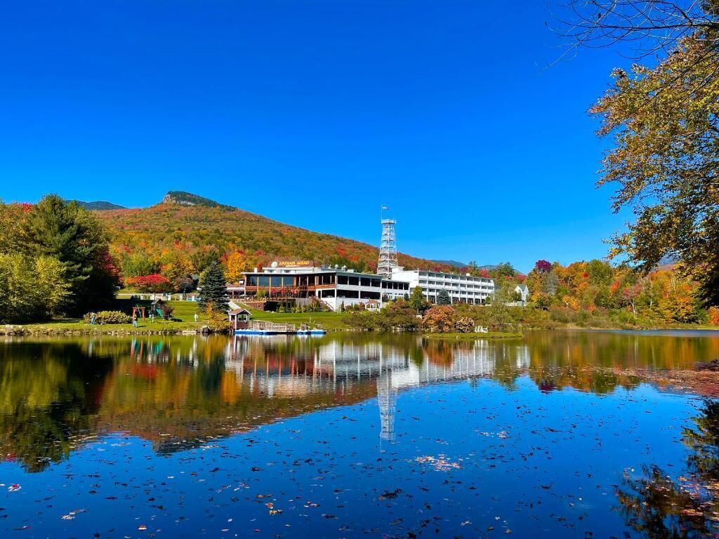A building with a tower, a lake, and autumn foliage.