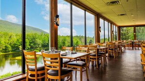 A restaurant with large windows offering a view of a lake and forest. Tables are arranged in rows with wooden chairs. - Indian Head Resort (Lincoln)