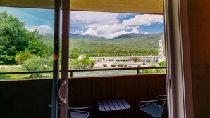 A balcony with a view of a tennis court, a building, and mountains. - Indian Head Resort (Lincoln)