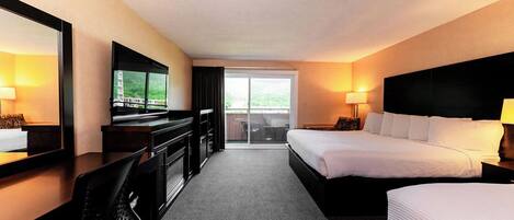 A hotel room with a bed, a desk, a TV, and a sliding door to a balcony.