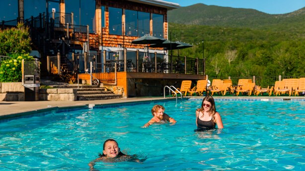 A swimming pool with a view of a building with large windows and outdoor seating. - Indian Head Resort (Lincoln)