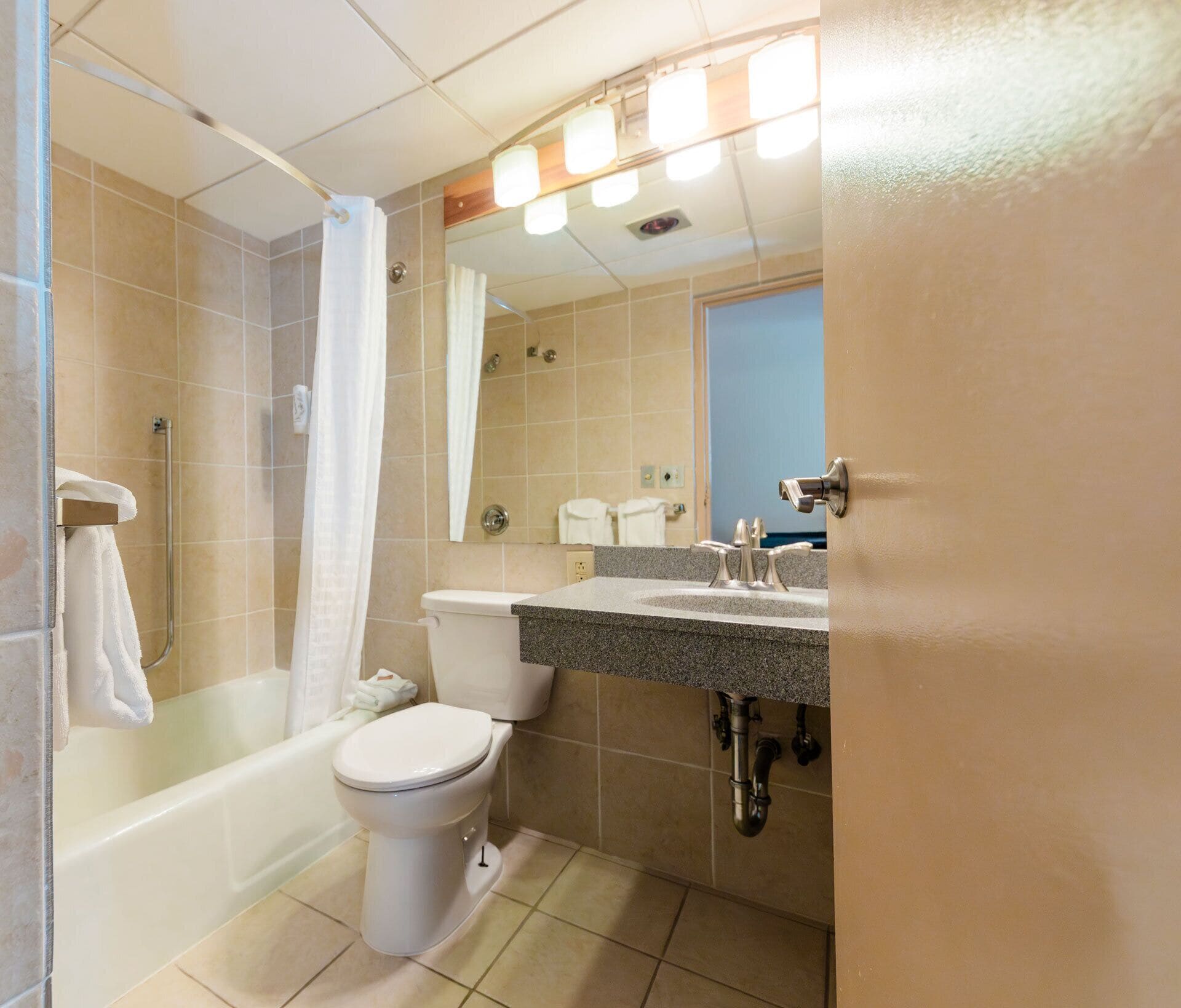 A bathroom with a shower, toilet, sink, and a mirror.