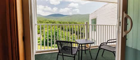 A balcony with a view of green hills, a white fence, and a small table and chair.