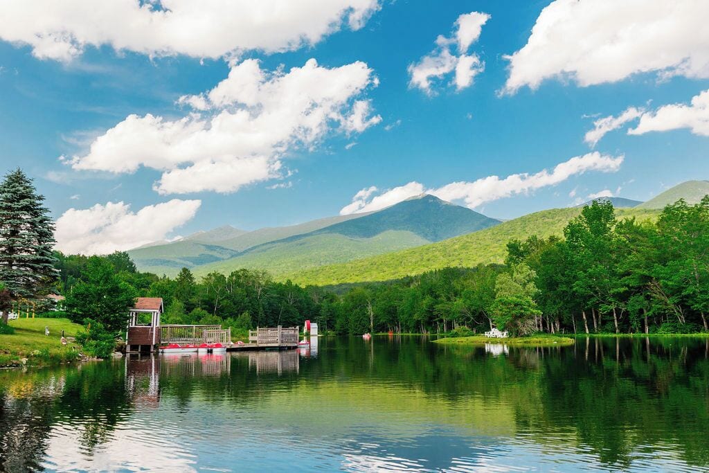 A serene lake with a dock, a small wooden structure, and lush greenery.