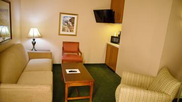 Habitación de hotel compacta con sofá, una mesita, una silla, un televisor montado en la pared y un microondas.