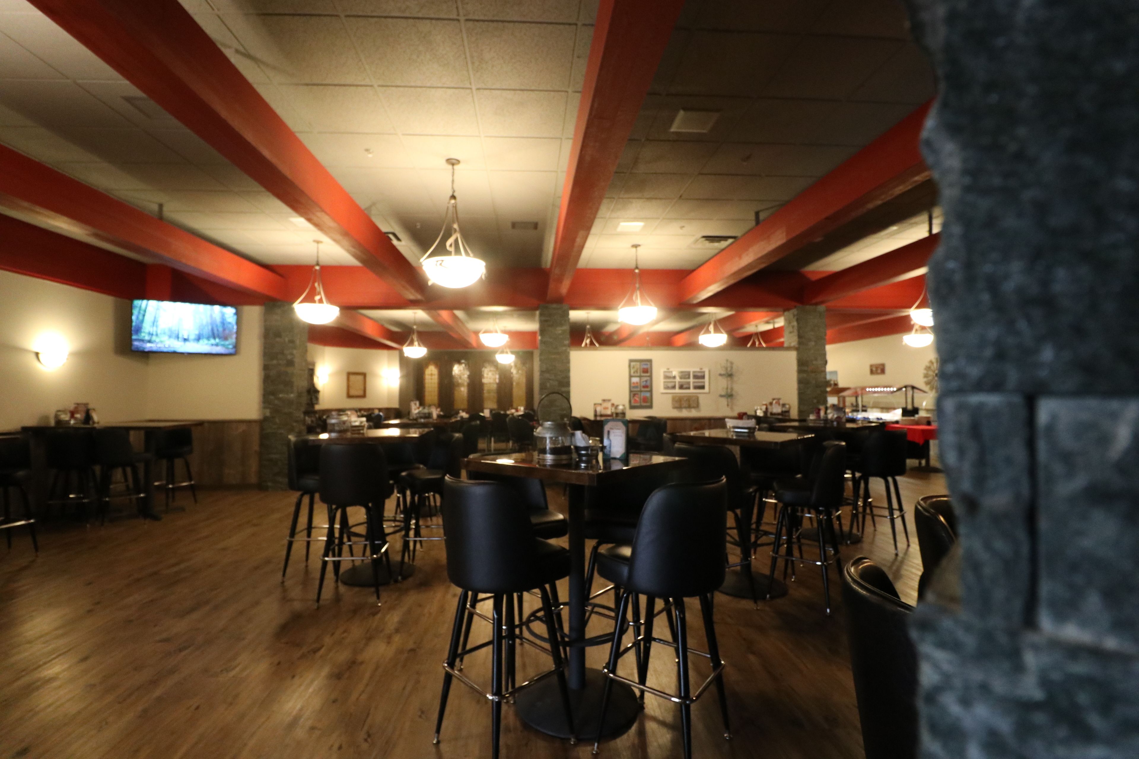 A restaurant with high ceilings, red beams, and multiple bar stools.