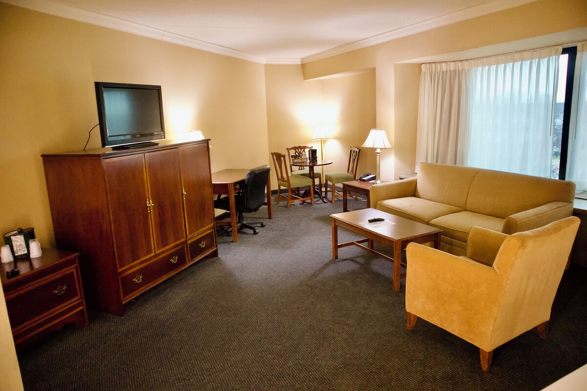 A hotel room with a wooden cabinet, a television, a sofa, a desk, and a chair.