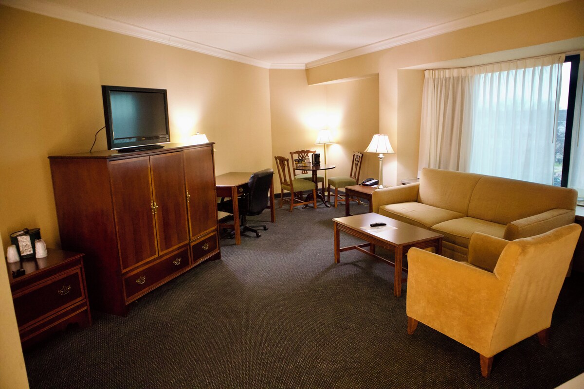 A hotel room with a sofa, armchair, desk, and television on a cabinet.