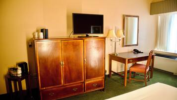 Habitación de hotel con un armario de madera, un escritorio con silla, televisor, lámpara y cama.