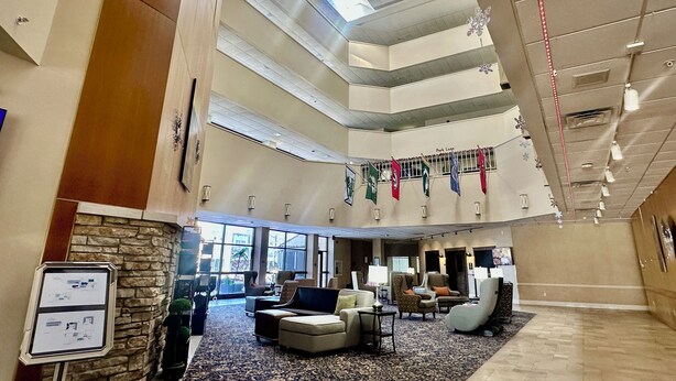 A spacious lobby with multiple seating areas, a stone accent wall, and a high ceiling with skylights. - Hotel Mead Resorts & Conventions Center (Wisconsin Rapids)