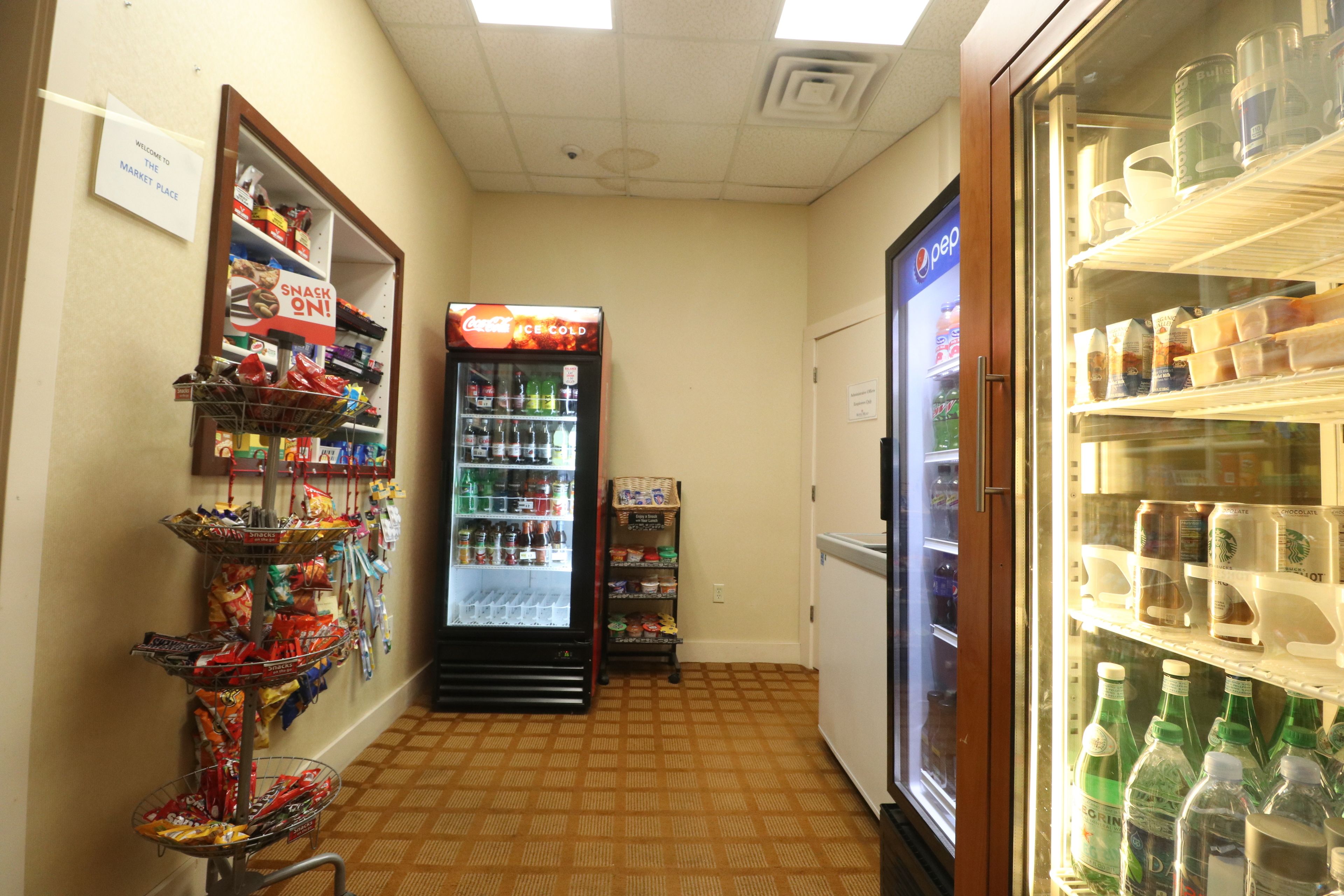 A corridor with a Coca-Cola refrigerator, snack vending machine, and a freezer stocked with beverages.