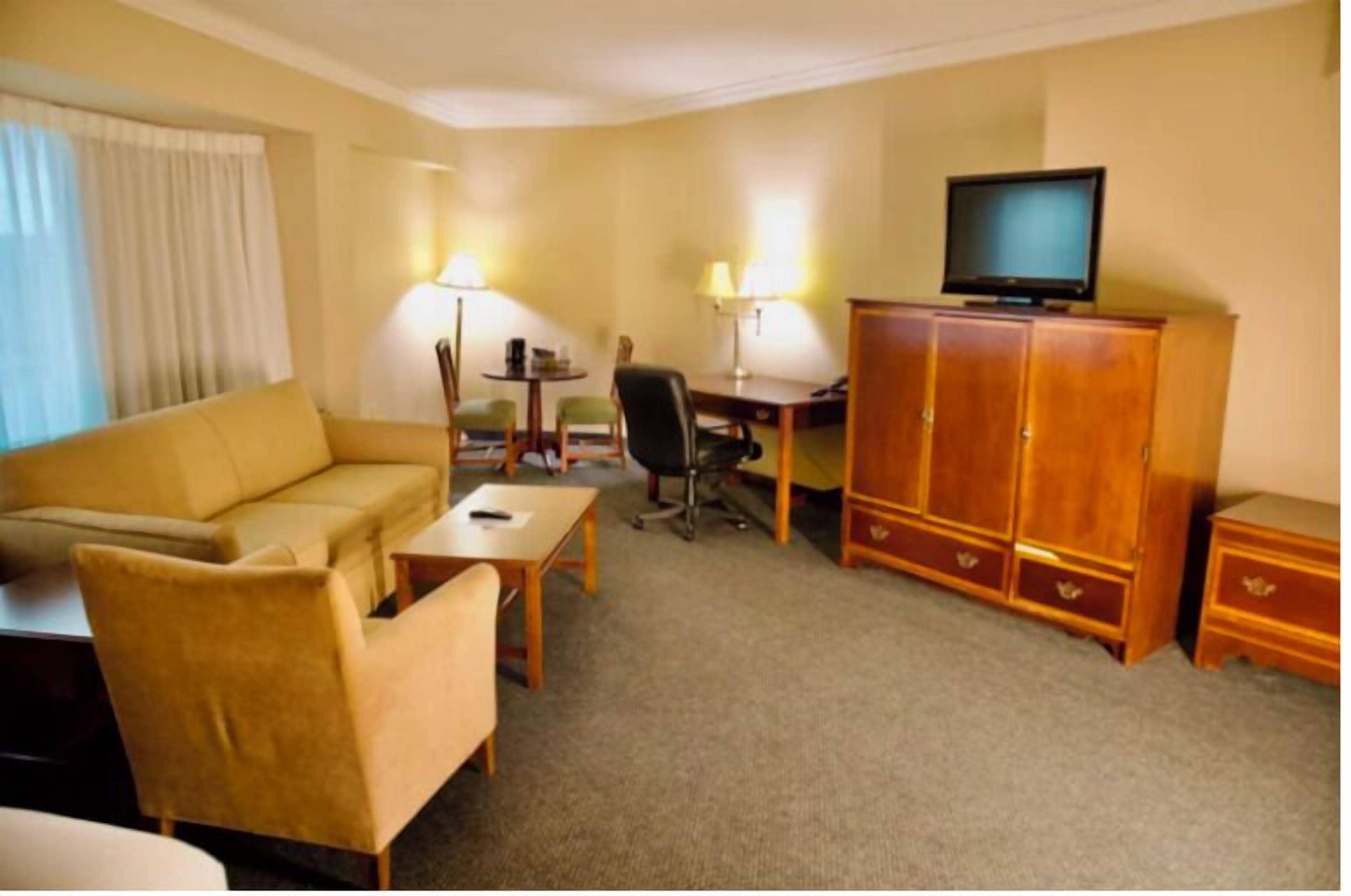 A hotel room with a sofa, a desk, a chair, a television, and a cabinet.