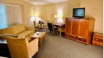 A hotel room with a sofa, a desk, a chair, a television, and a cabinet.